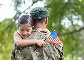 child holding a flag hugging a soldier