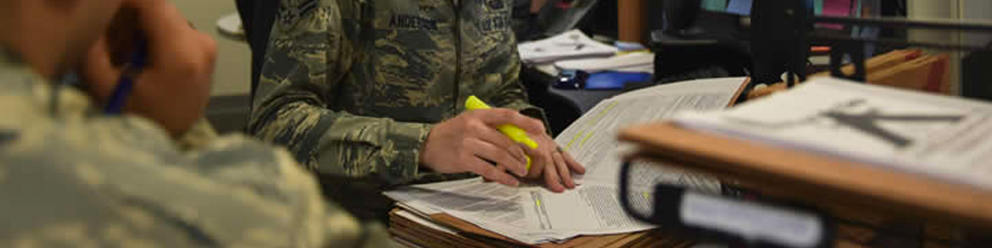 person in military uniform highlighting papers on a desk